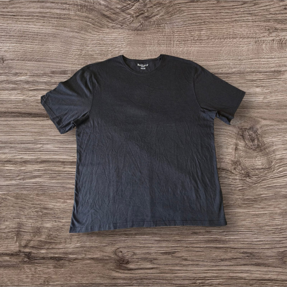 T-shirt nera a maniche corte Ottoman Kumus Bexleys MAN in cotone morbido con girocollo su sfondo in legno