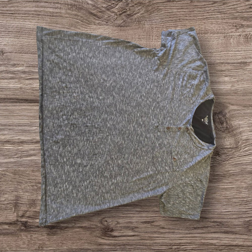 T-shirt henley Ottoman Kumus grigia mélange con taschino sul petto e chiusura a tre bottoni su sfondo in legno