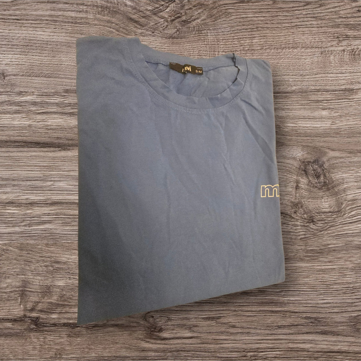 T-shirt Mavi grigio-azzurra in cotone con logo ricamato, proposta da Ottoman Kumus su sfondo in legno.