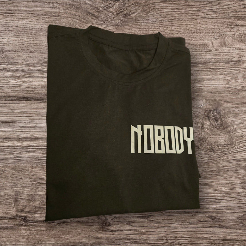 T-shirt nera in cotone Ottoman Kumus con scritta Nobody bianca sul petto, stile streetwear piegata su legno