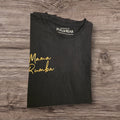 T-shirt nera Ottoman Kumus PULL&BEAR in cotone con scritta Mama Rumba dorata sul petto, piegata su sfondo in legno.